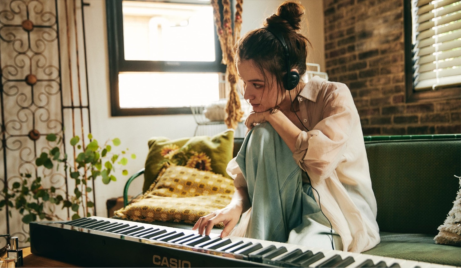 Девушка играет на чёрном Casio PX-S1100 в проводных наушниках дома — виден плоский тонкий корпус пианино