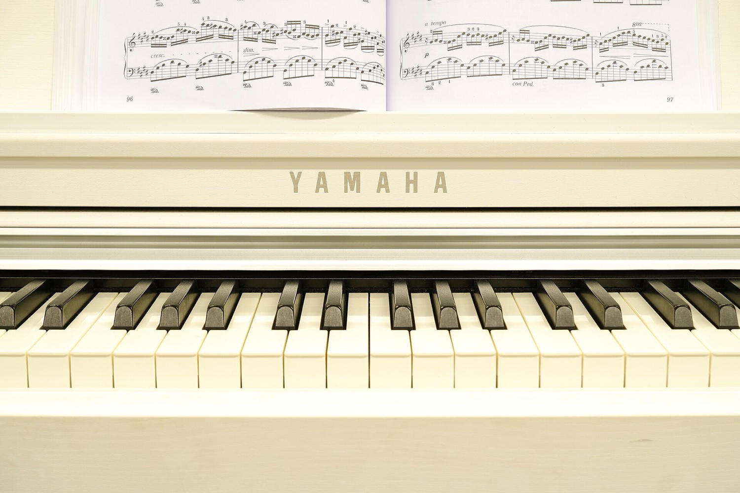 Крупный план клавиш цифрового пианино Yamaha с логотипом на корпусе и раскрытыми нотами на пюпитре