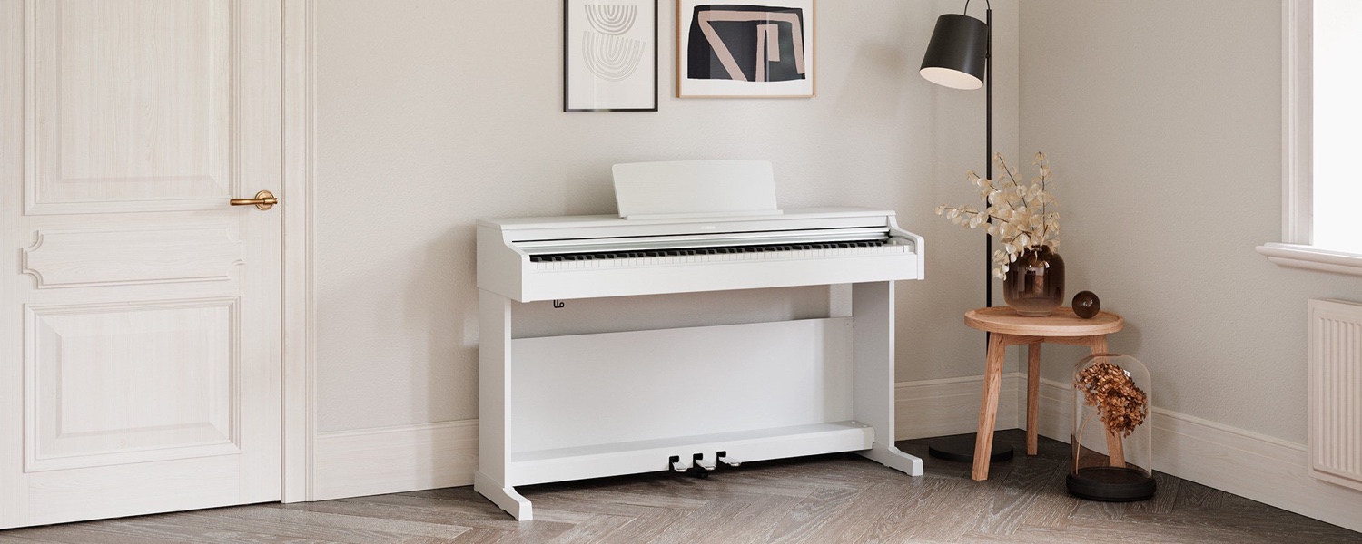 Белое корпусное цифровое пианино Yamaha Arius YDP-165 в исполнении WH у стены светлой комнаты: закрытая крышка клавиатуры, пюпитр, три педали; рядом дверь, торшер и столик с сухоцветами