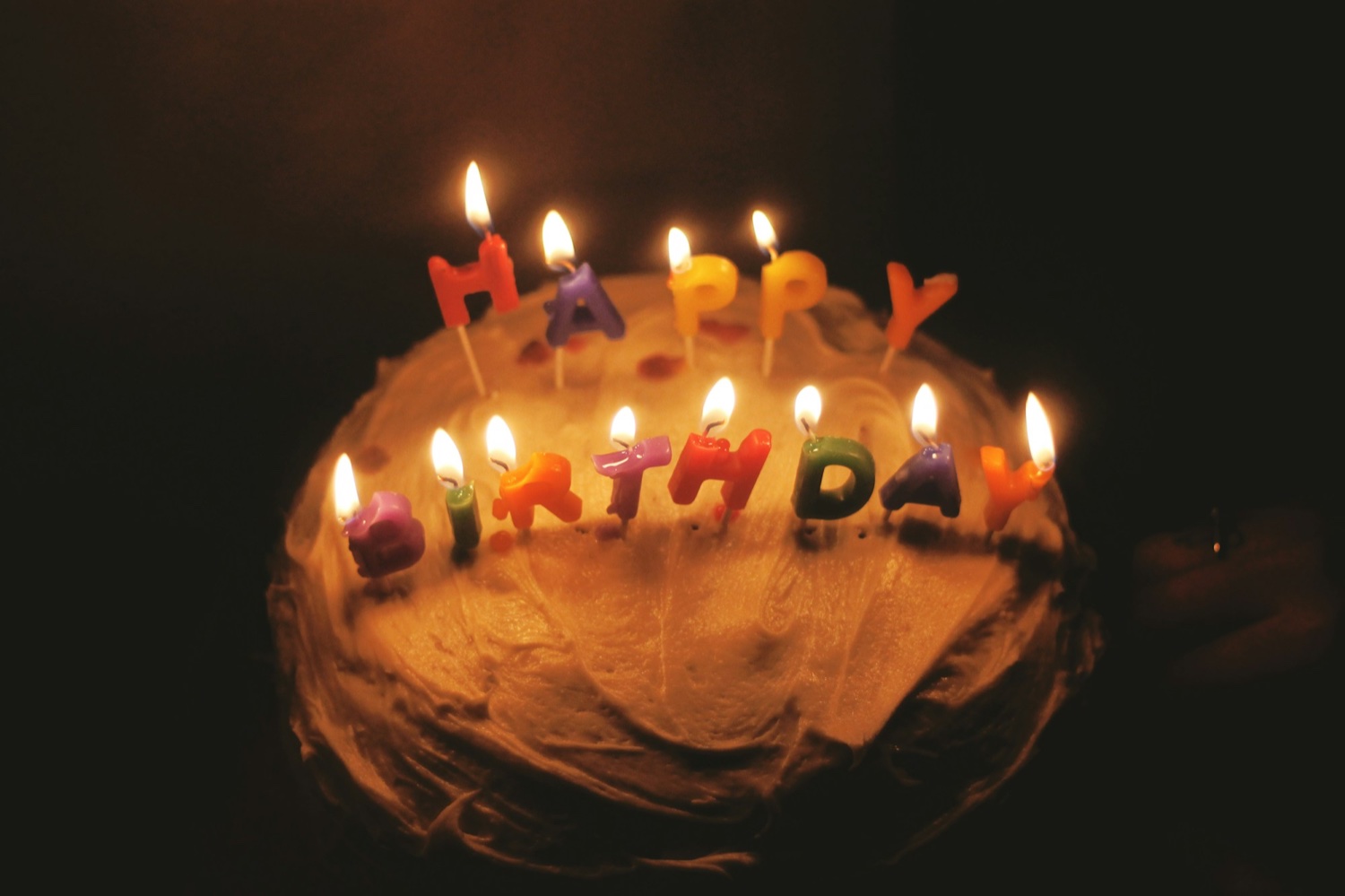 Праздничный торт со свечами-буквами HAPPY BIRTHDAY, горящими в полутёмной комнате
