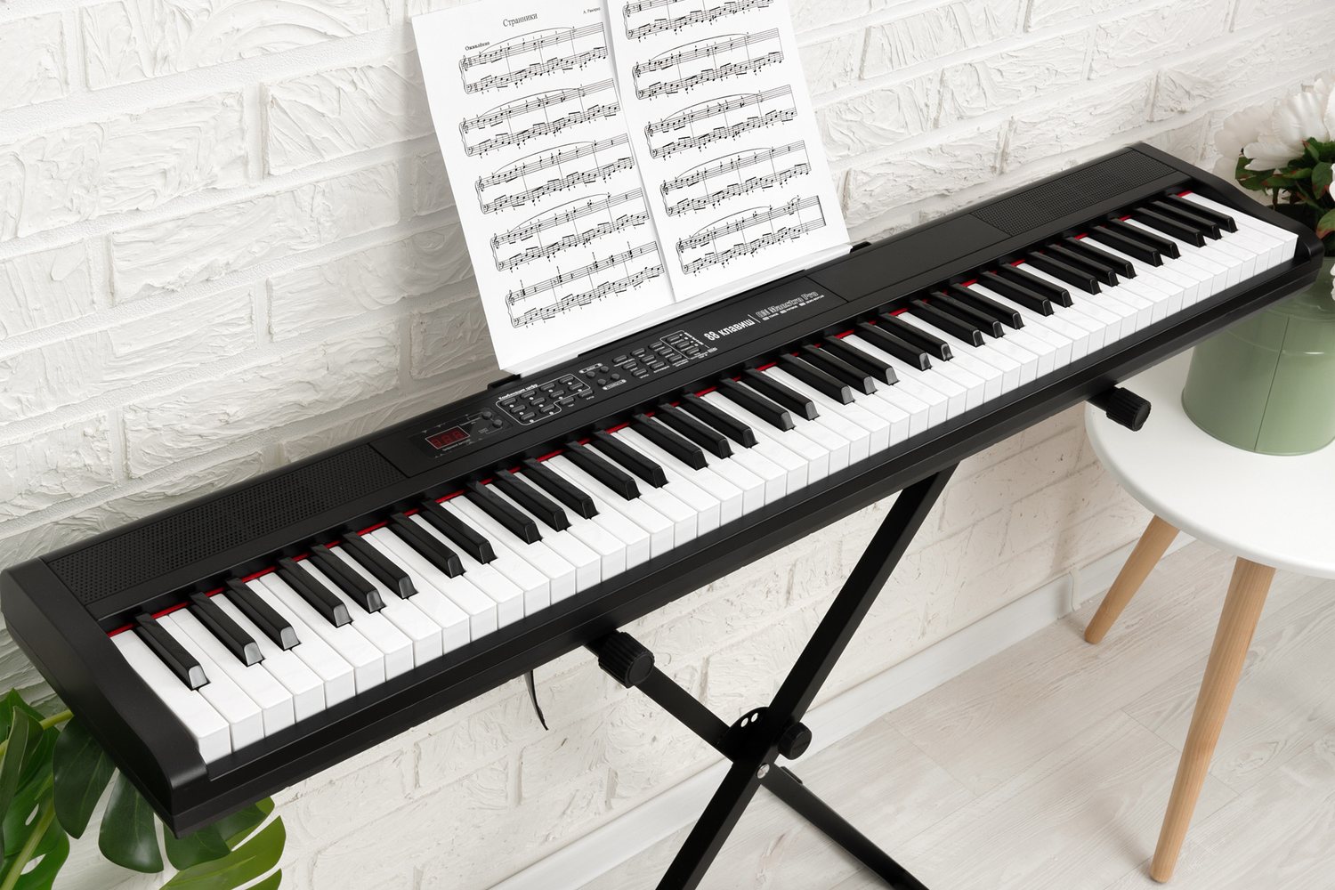 ON Music Maestro Pro на X-образной стойке у кирпичной стены: 88 клавиш, панель с дисплеем и кнопками, ноты на пюпитре