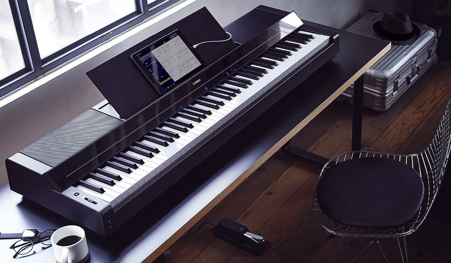 Цифровое пианино Yamaha P-S500 на столе у окна: на пюпитре планшет с нотами, над клавишами светятся красные и синие огоньки подсказки