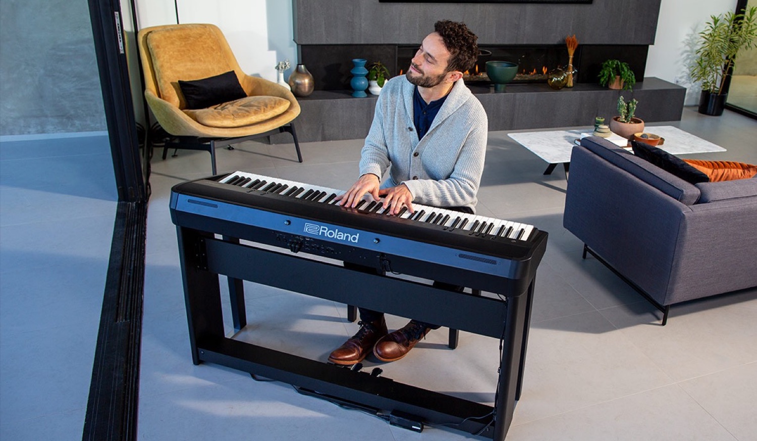 Чёрное цифровое пианино Roland FP-90X на фирменной стойке с педальным блоком в светлой гостиной, за инструментом сидит мужчина