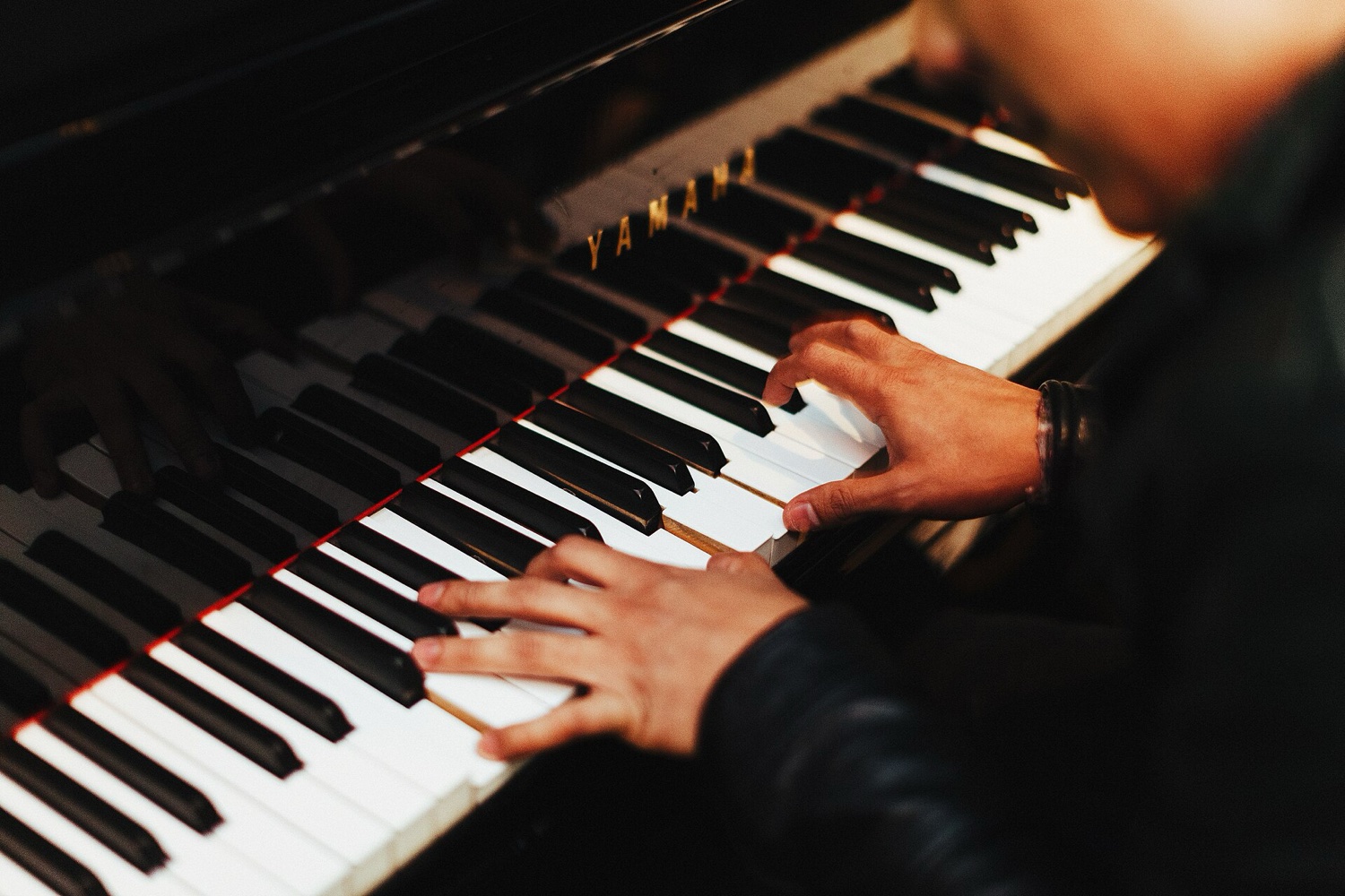 Руки пианиста на клавиатуре рояля Yamaha: правая рука в верхнем регистре, левая ниже, крупный план в тёплом свете