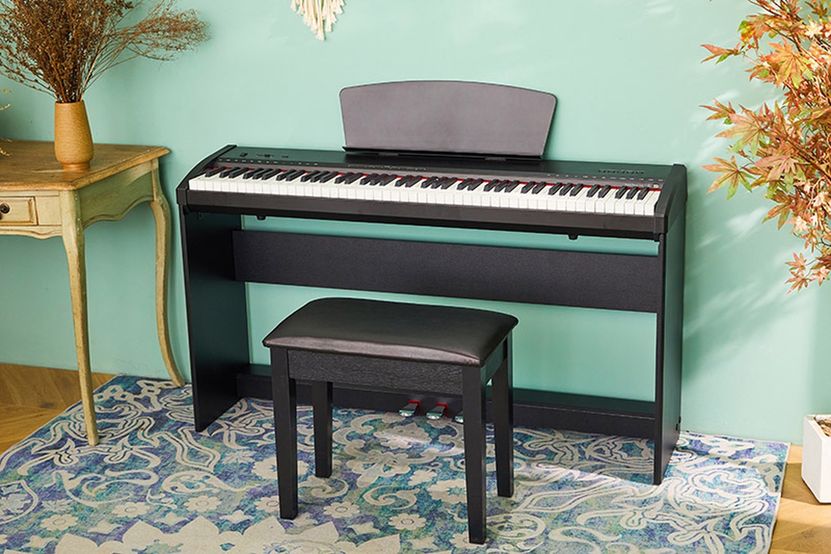Чёрное корпусное цифровое пианино Sai Piano P-9BT-BK с пюпитром и тремя педалями у мятной стены, перед ним банкетка на узорном ковре