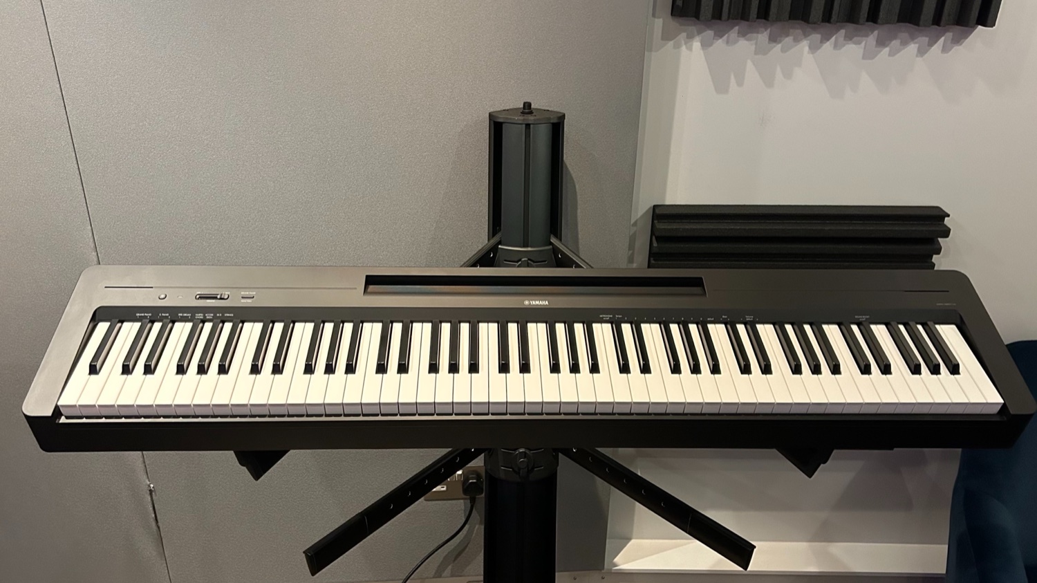 Чёрное портативное цифровое пианино Yamaha P-145 на прямой стойке в студии с акустическими панелями на стене