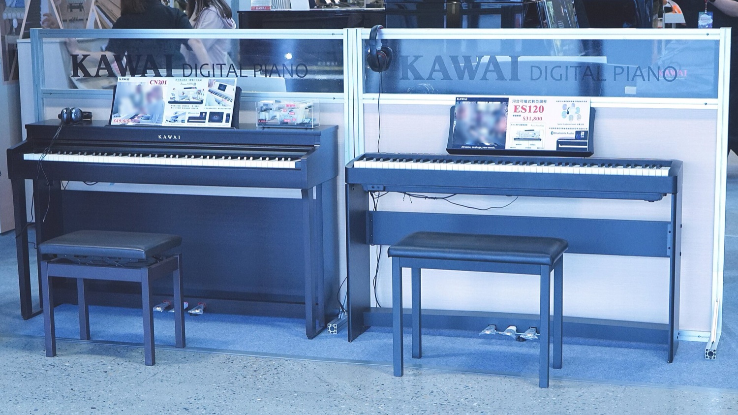 Корпусное цифровое пианино Kawai CN201 с банкеткой и рядом портативное Kawai ES120 на стойке с педальным блоком, витрина магазина с ценниками