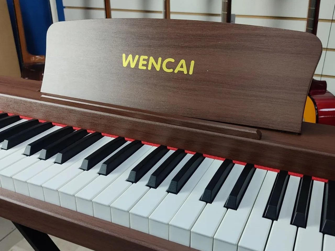 Клавиатура Wencai BL-280 под углом: белые и чёрные клавиши полноразмерного 88-клавишного портатива, красный фетр вдоль задней кромки, пюпитр из ДСП под тёмное дерево с жёлтой надписью WENCAI