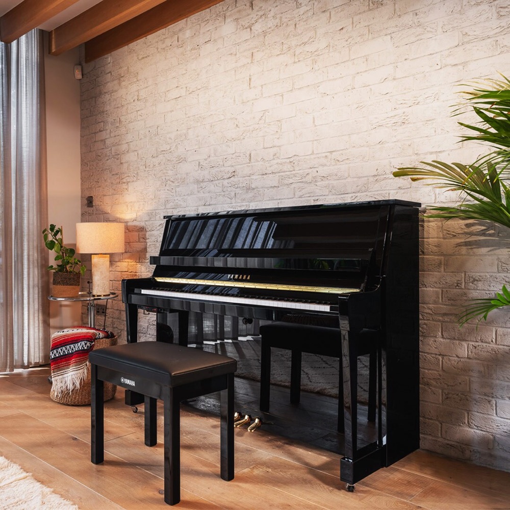 Чёрное акустическое вертикальное пианино Yamaha b-серии с банкеткой у кирпичной стены в интерьере