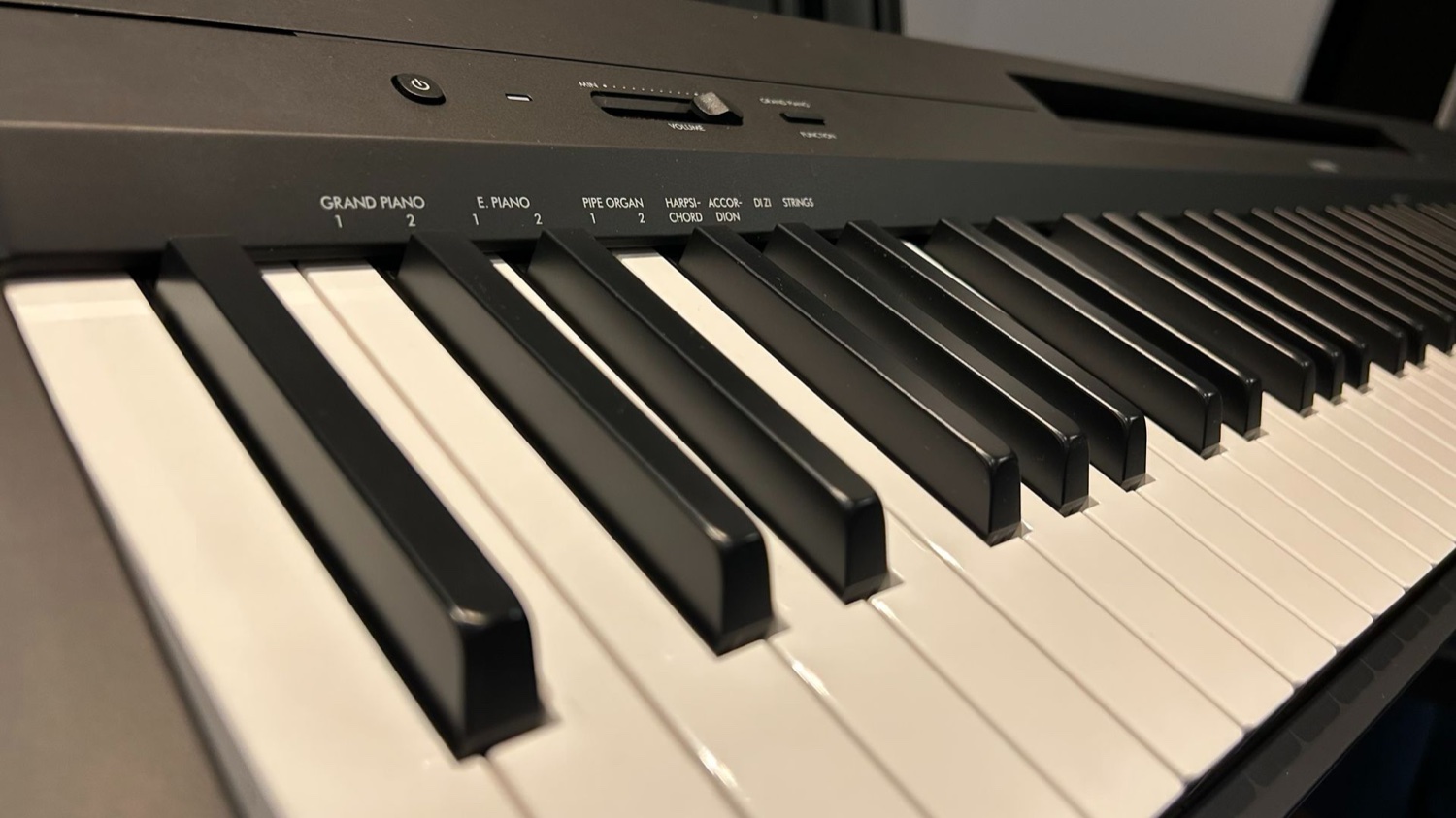 Левый край панели Yamaha P-145: кнопка питания, слайдер громкости и напечатанные над клавишами названия тембров — GRAND PIANO, E.PIANO, PIPE ORGAN, STRINGS